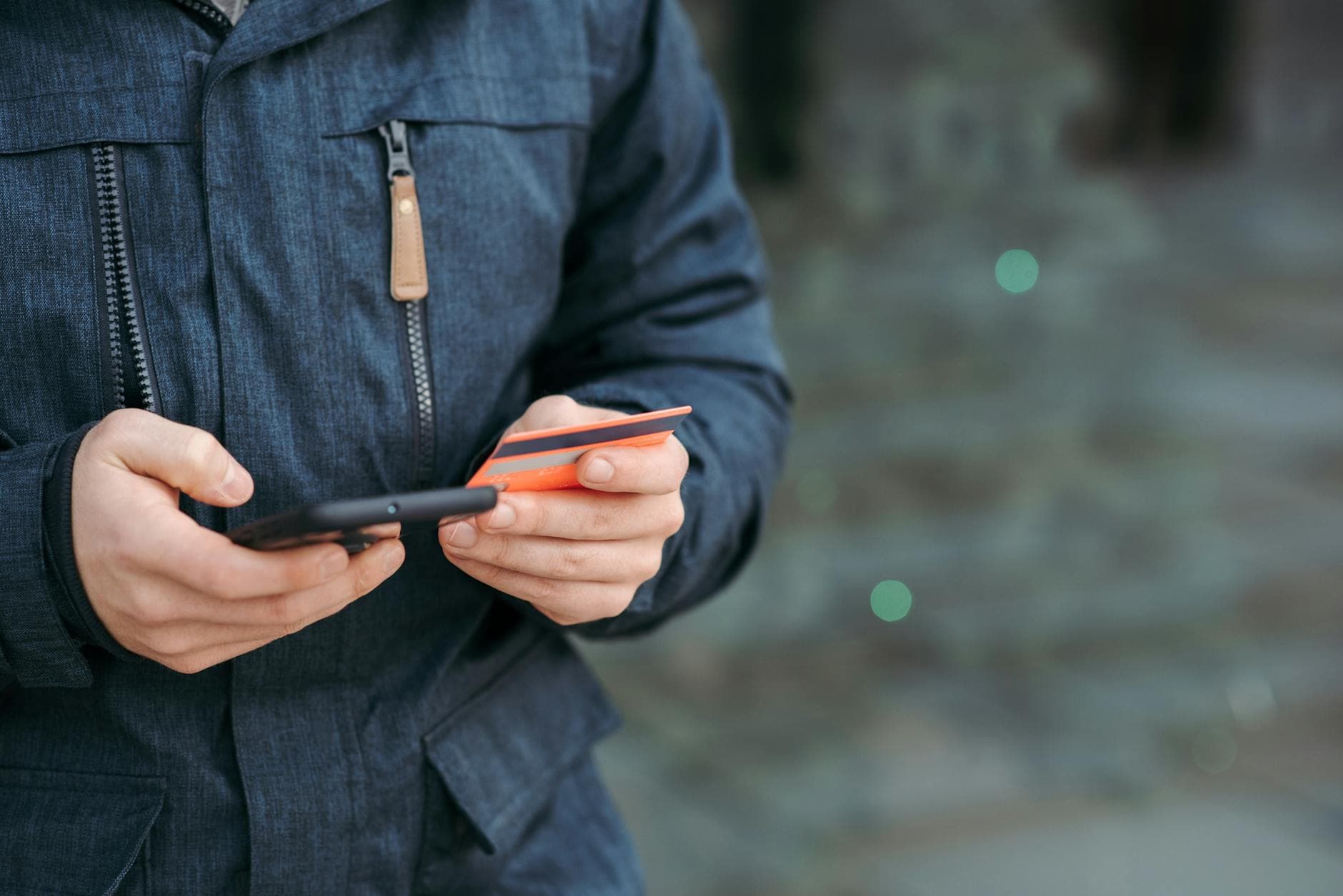 Crop anonymous male in casual clothes entering credit card details on smartphone on street in daylig