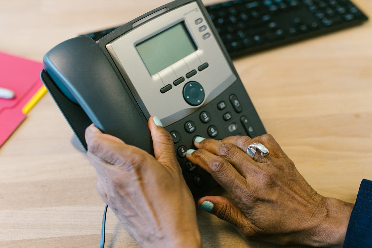 Close-up of an agent's hands dialling a desk telephone keypad in a contact-centre office