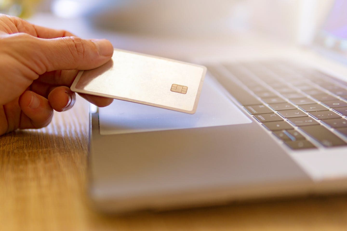 A person holds a credit card near a laptop for online shopping.