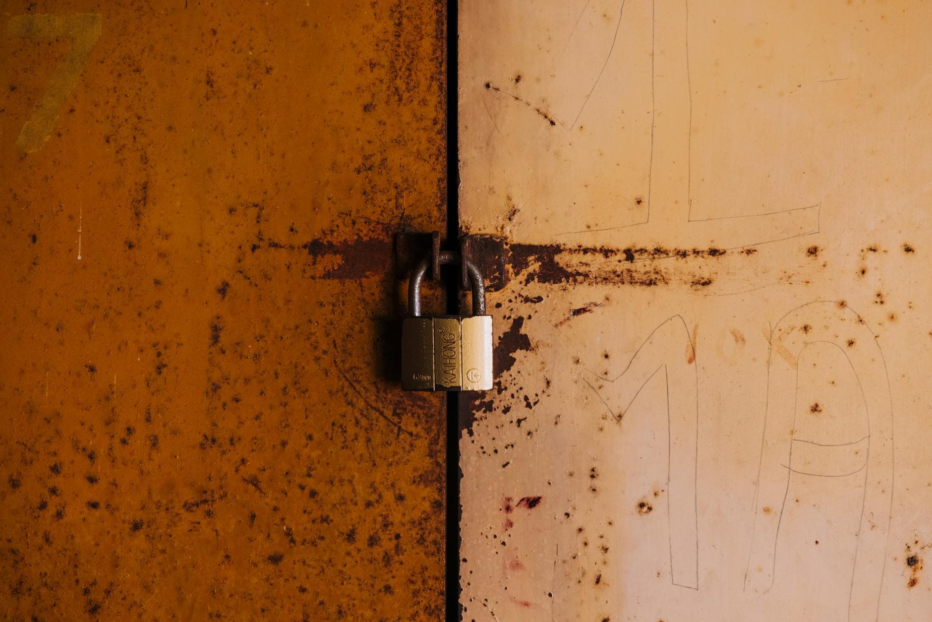 A close-up view of a rusty padlock securing a weathered metal door, highlighting decay and security.
