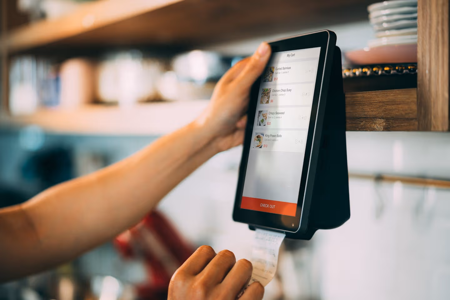 A hand uses a touchscreen digital payment system to process a receipt at a cafe.