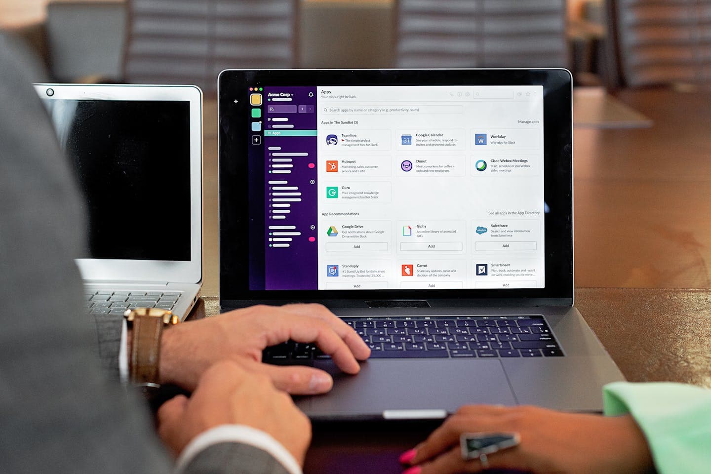 Two professionals collaborating using laptops and communication software in a business setting.