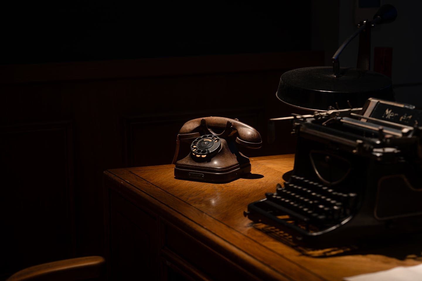 A dimly lit vintage office desk featuring a rotary telephone and typewriter.