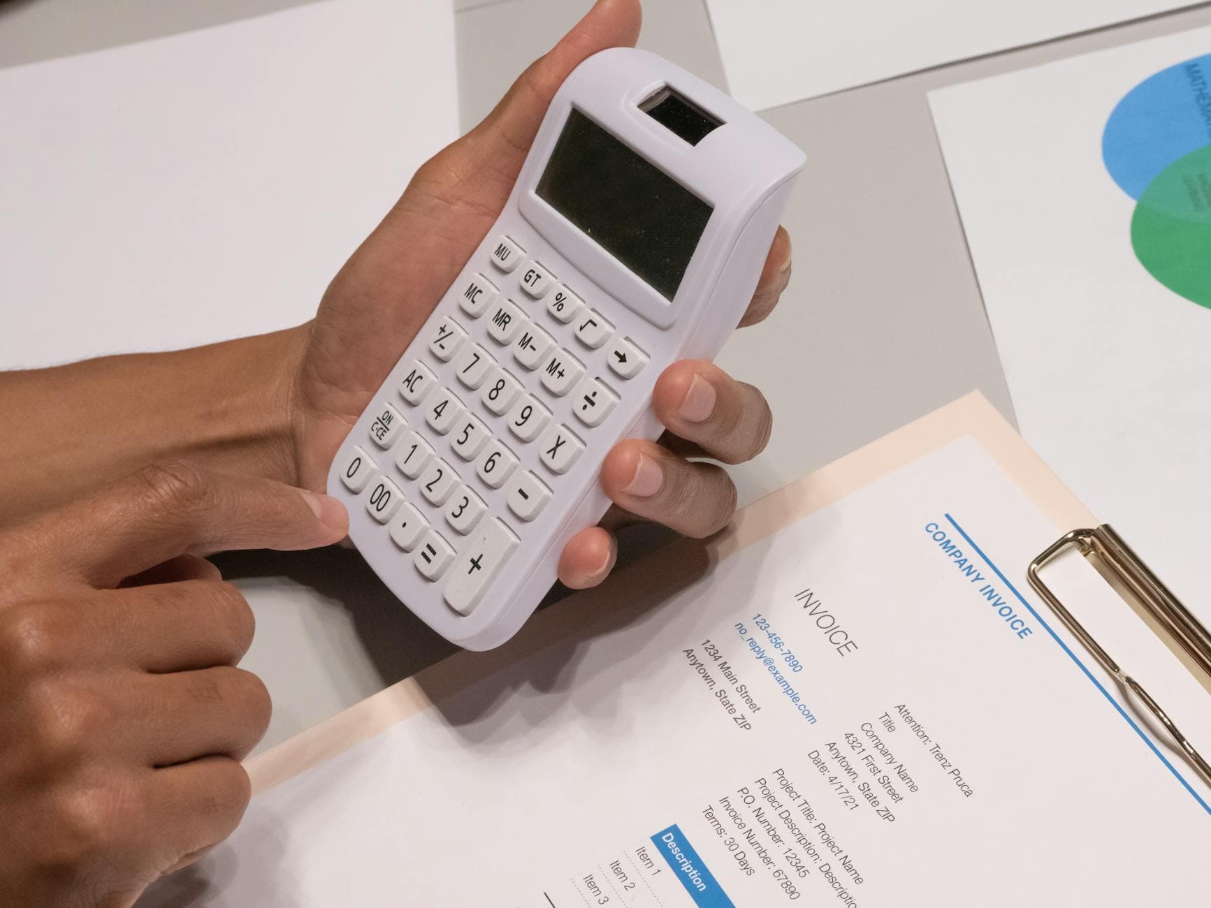 Close-up of hands using a calculator next to a printed business invoice on a desk