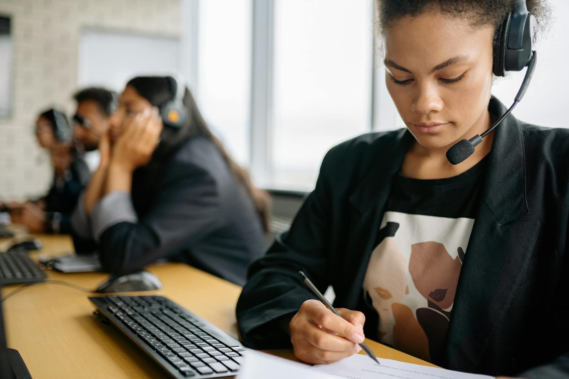 Focused call center employee using headset and writing notes at her desk, working efficiently.