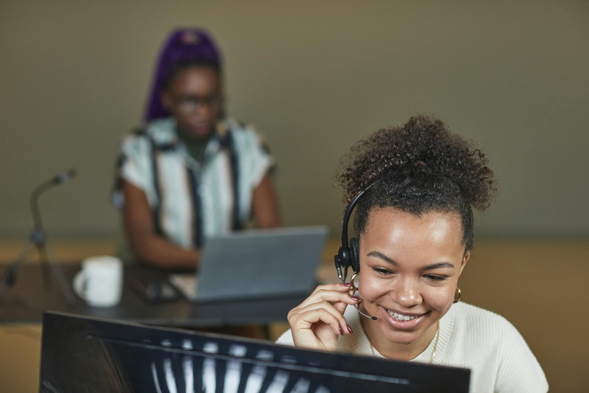 Smiling woman wearing a headset working at a call center desk with laptop.