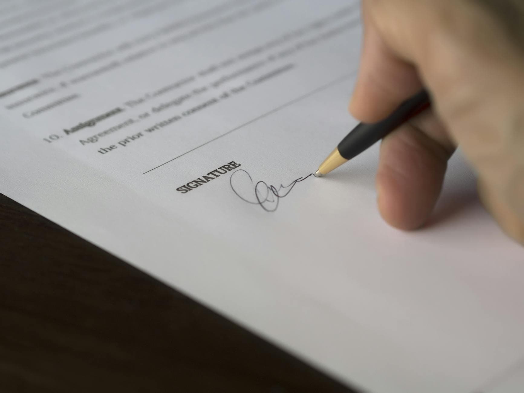 Hand signing a formal contract with a pen on a wooden desk, representing written consumer consent