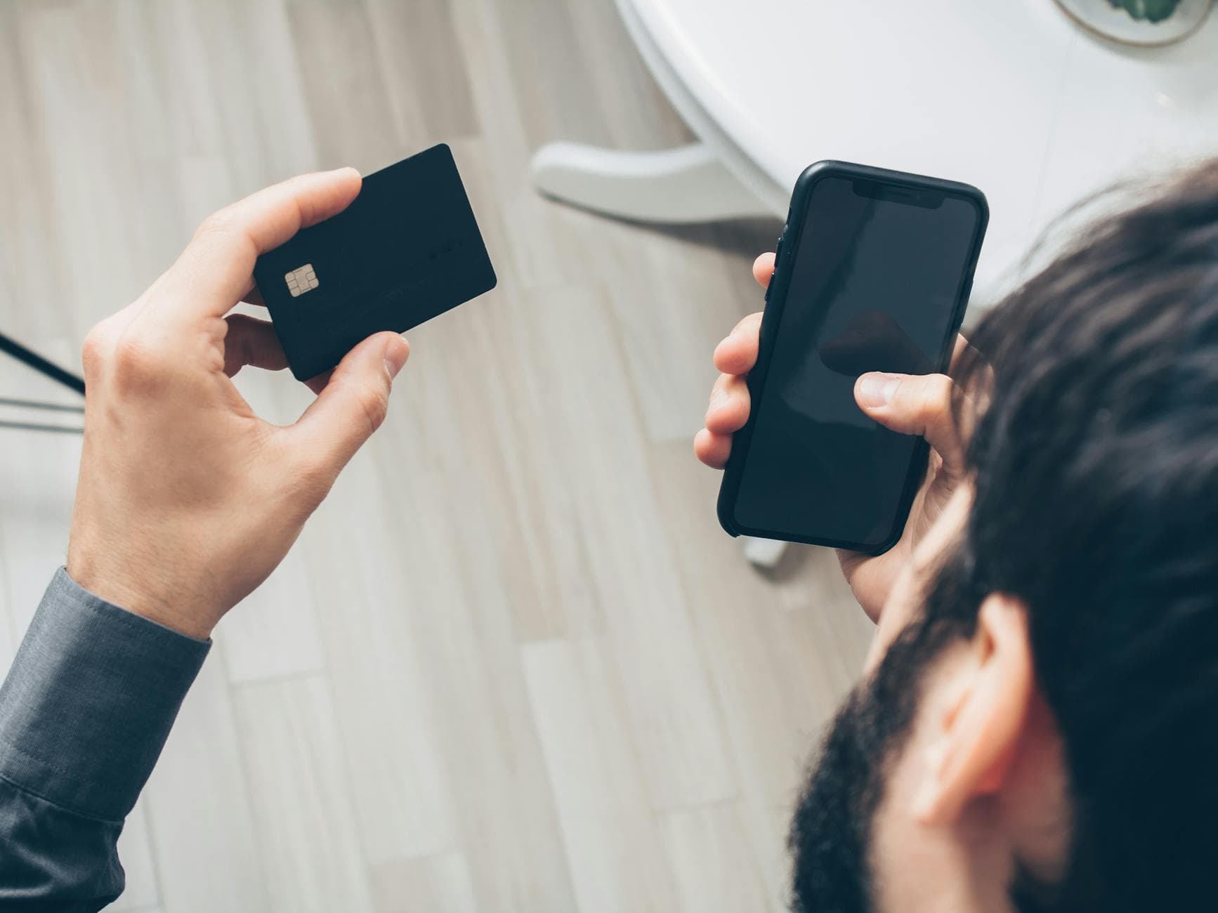Close-up of a man holding a smartphone and credit card while making a payment indoors