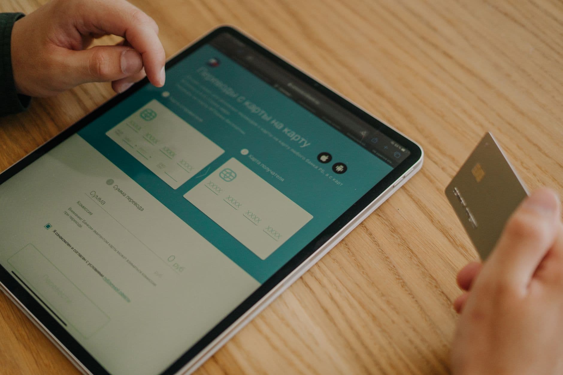 Hands using a tablet and credit card on a wooden table