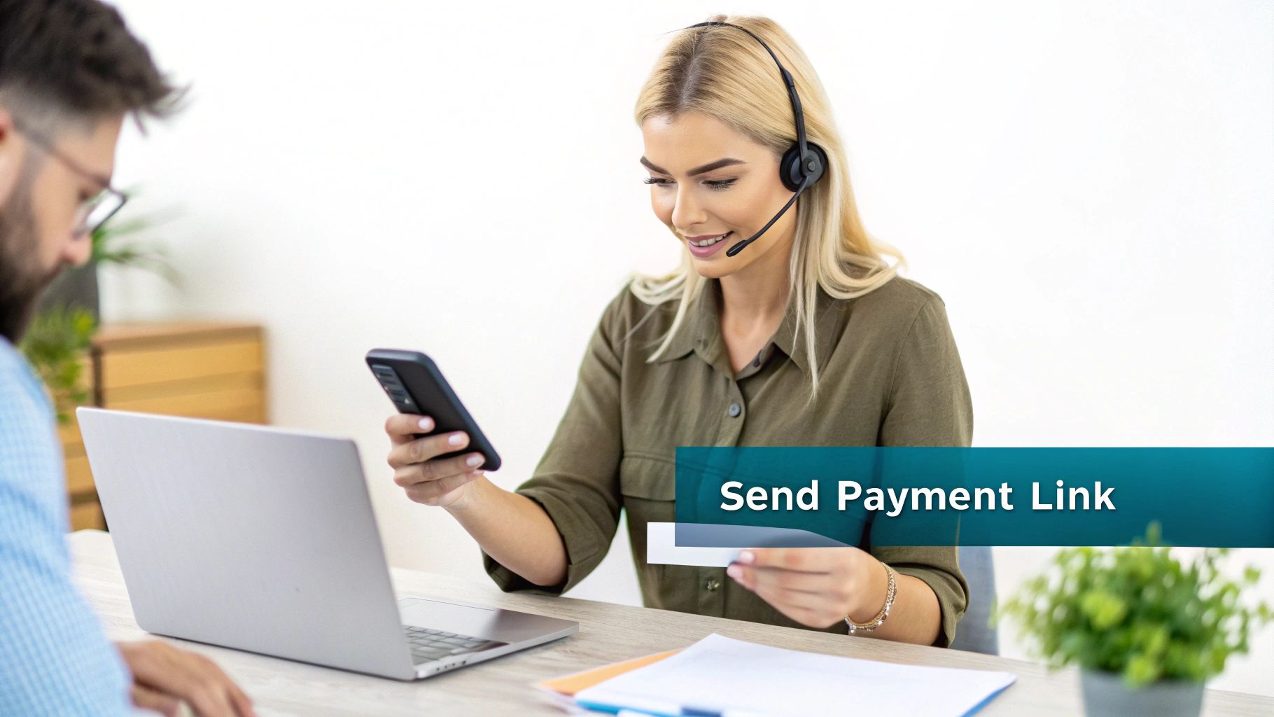 A smiling woman with a headset looks at her smartphone, holding a payment card.