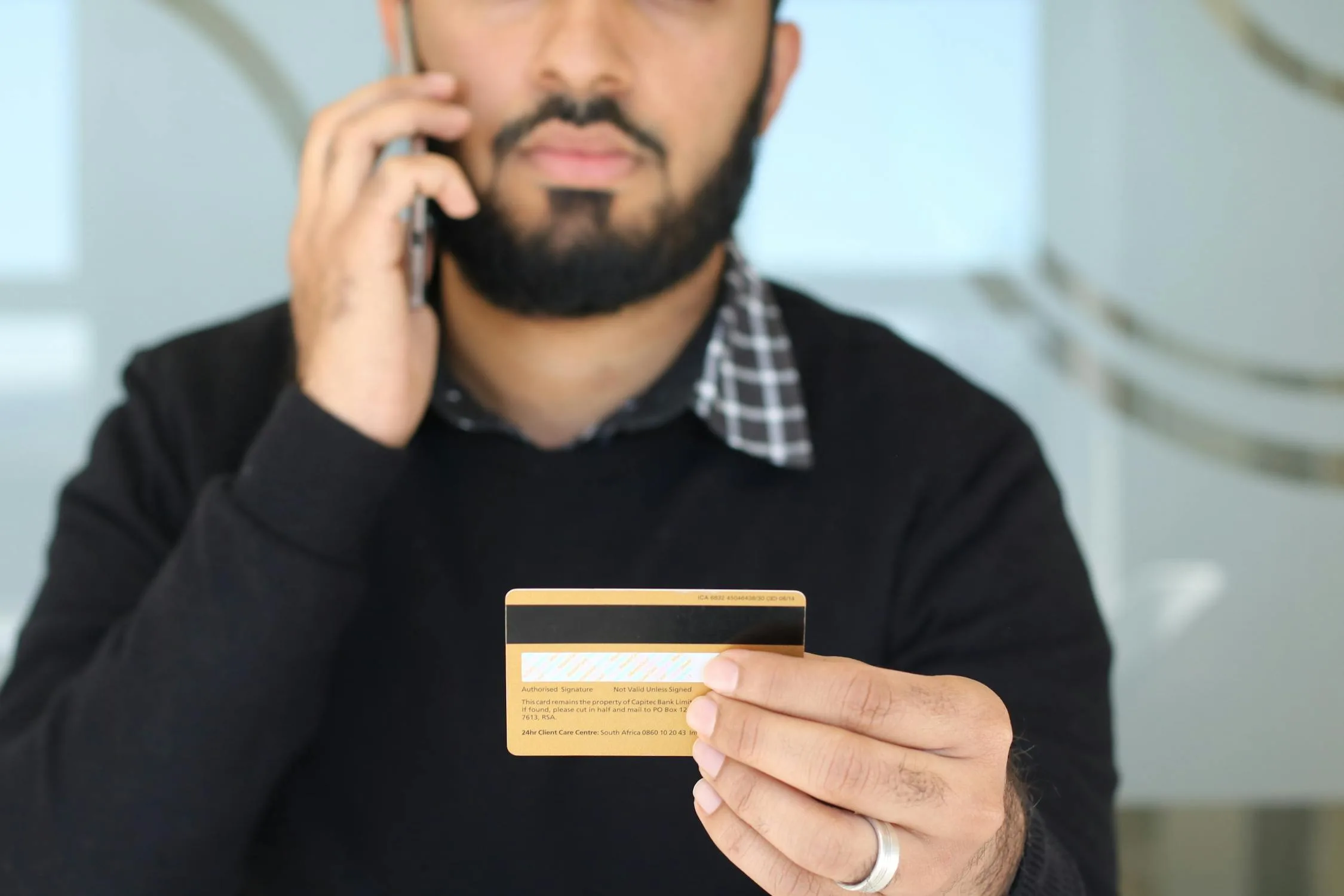 Customer holding a credit card while speaking on the phone — the moment when ProxyPay captures the card data securely without it reaching the business